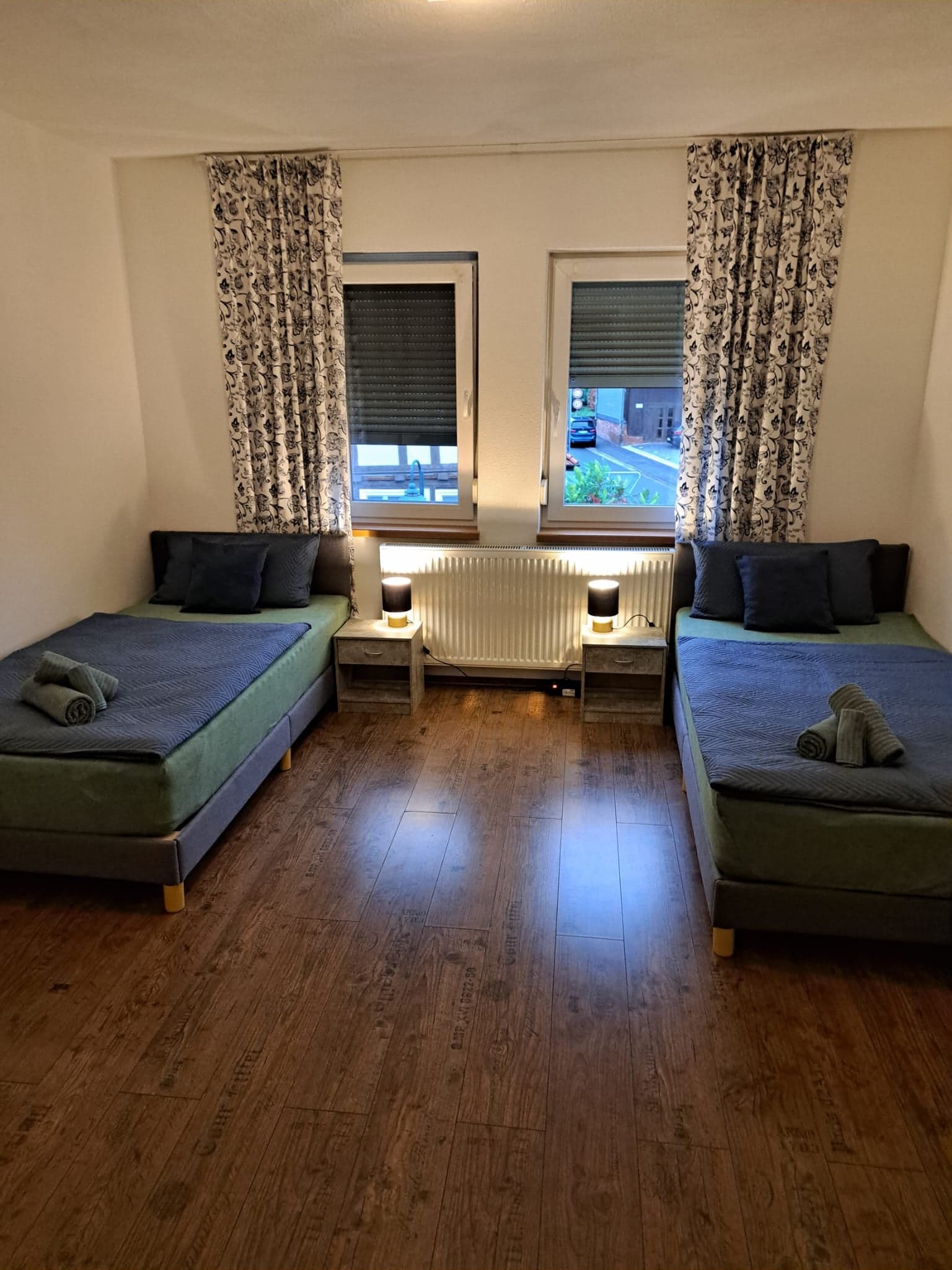 Zimmer der Wohnung A mit zwei Einzelbetten, Nachttischen und warmen Tischlampen