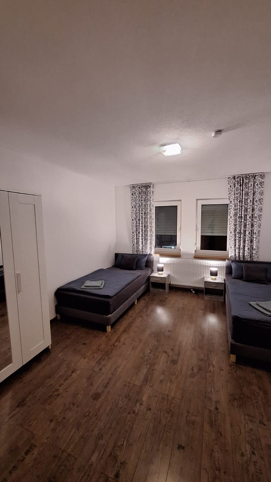 Dasselbe Zimmer der Wohnung A am Abend, mit zwei Einzelbetten und weißem Kleiderschrank