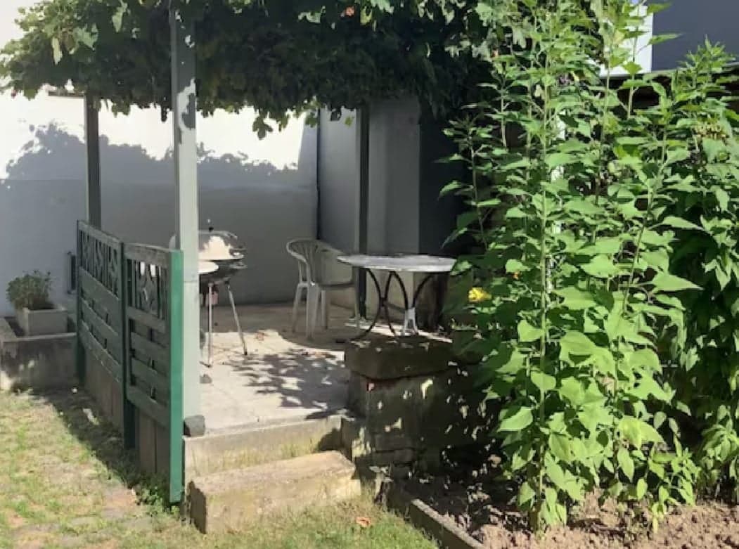 Begrünte Pergola an der Wohnung A mit Sitzplatz, Gartentisch und Grill im Schatten