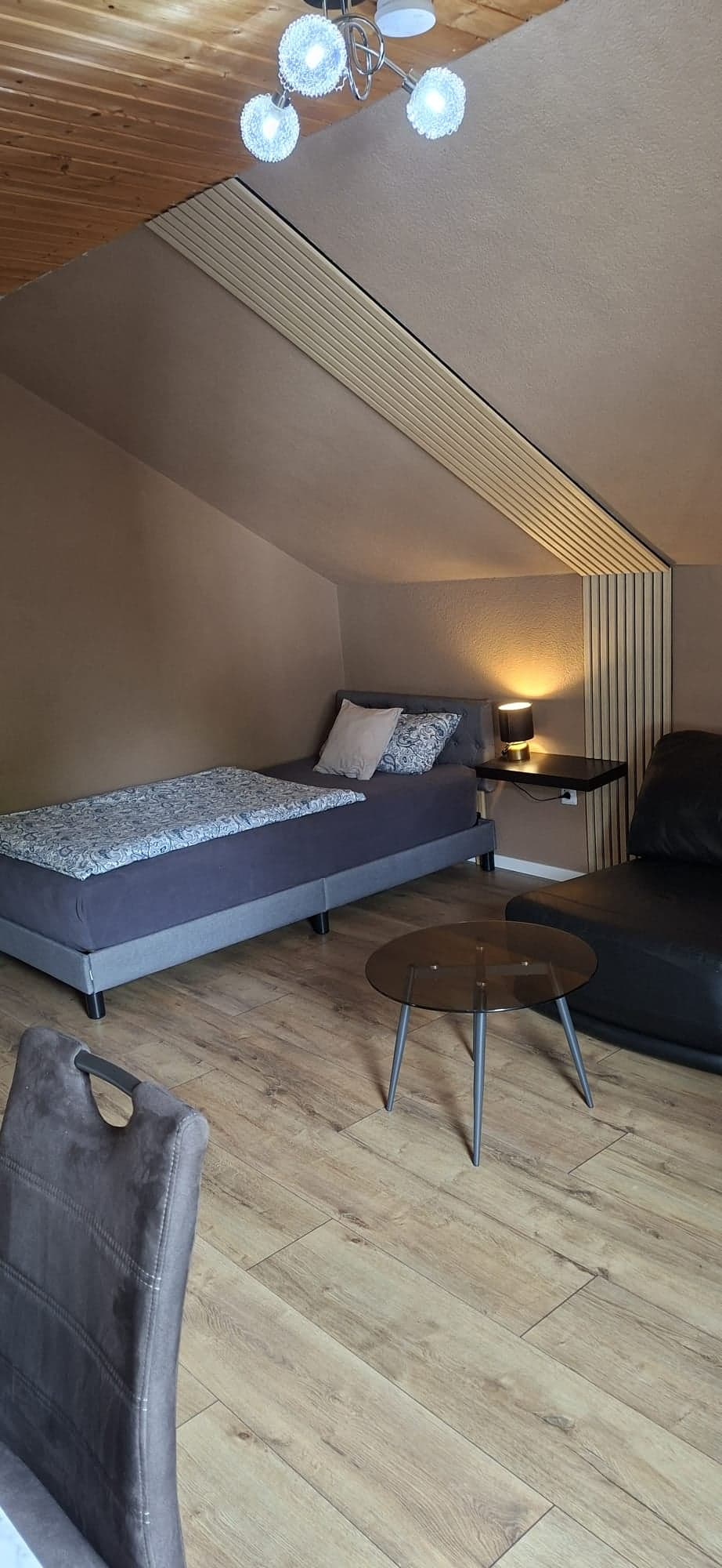 Derselbe Raum der Wohnung B mit Einzelbett, Wandregal mit Leselampe und Glastisch