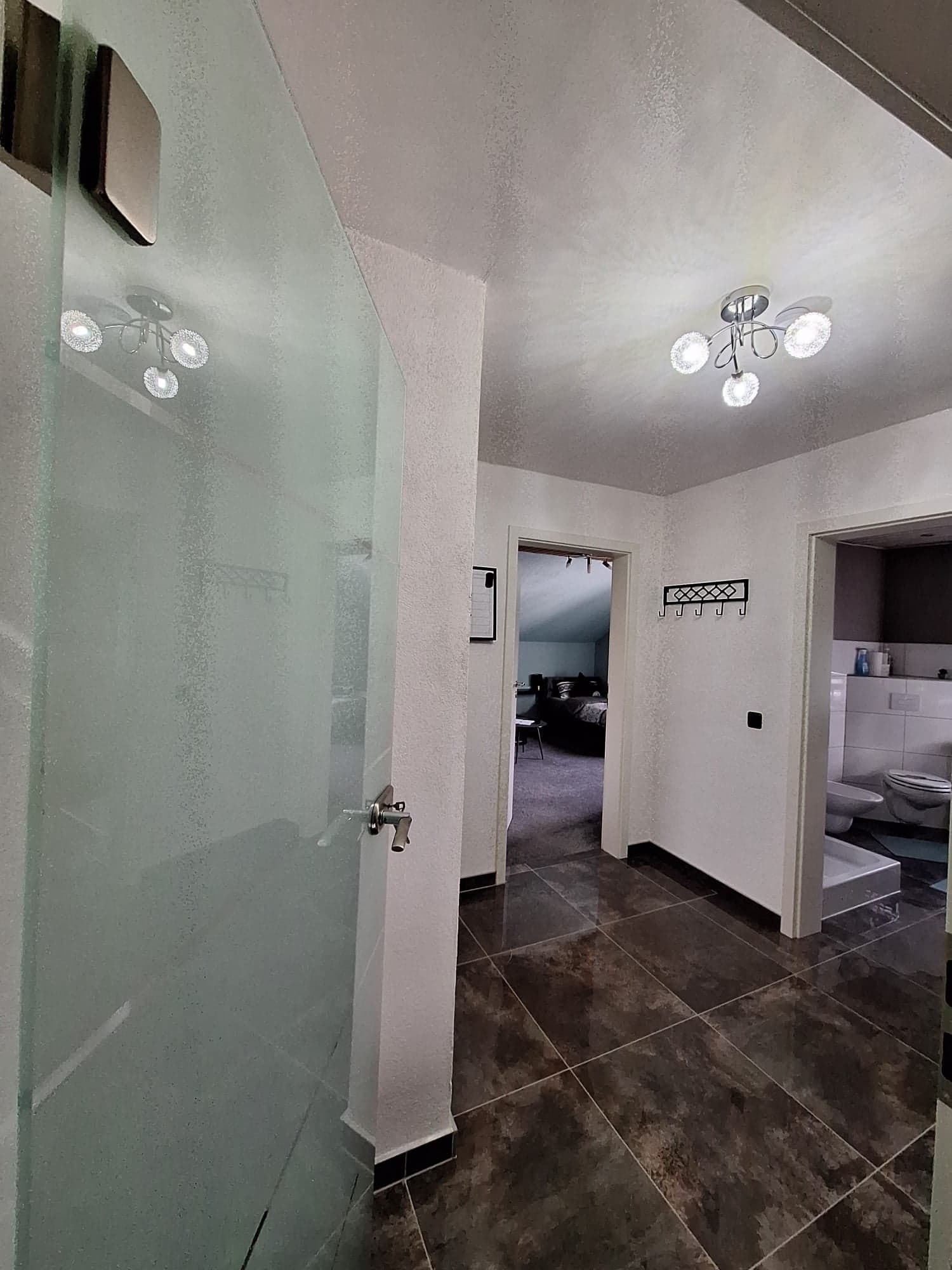 Flur der Wohnung B mit dunklen Fliesen, Glastür und Blick ins Badezimmer