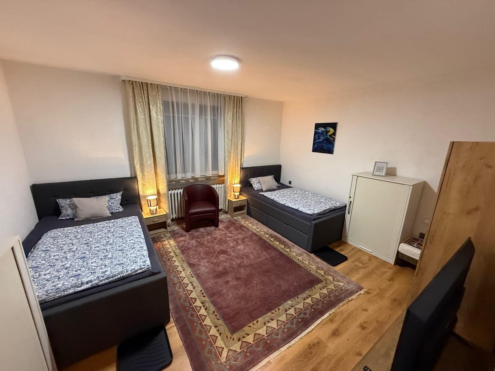 Zimmer der Wohnung C mit zwei Einzelbetten, rotem Ledersessel und warmen Nachttischlampen